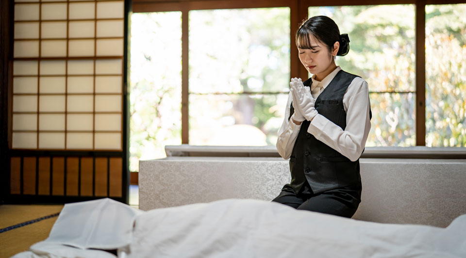 大田区葬儀相談室のスタッフが和室で白装布の遺体に手を合わせる直葬プラン案内写真