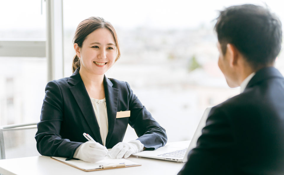 大田区葬儀相談室のスタッフが搬送対応を説明しながら笑顔で受付する場面、搬送・葬儀相談の案内として適用される