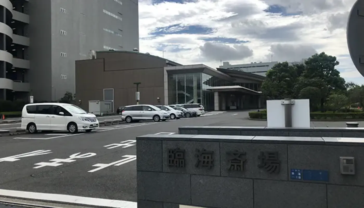 大田区葬儀相談室が臨海斎場の入口前に並ぶ車と建物を背景にした斎場外観を撮影している
